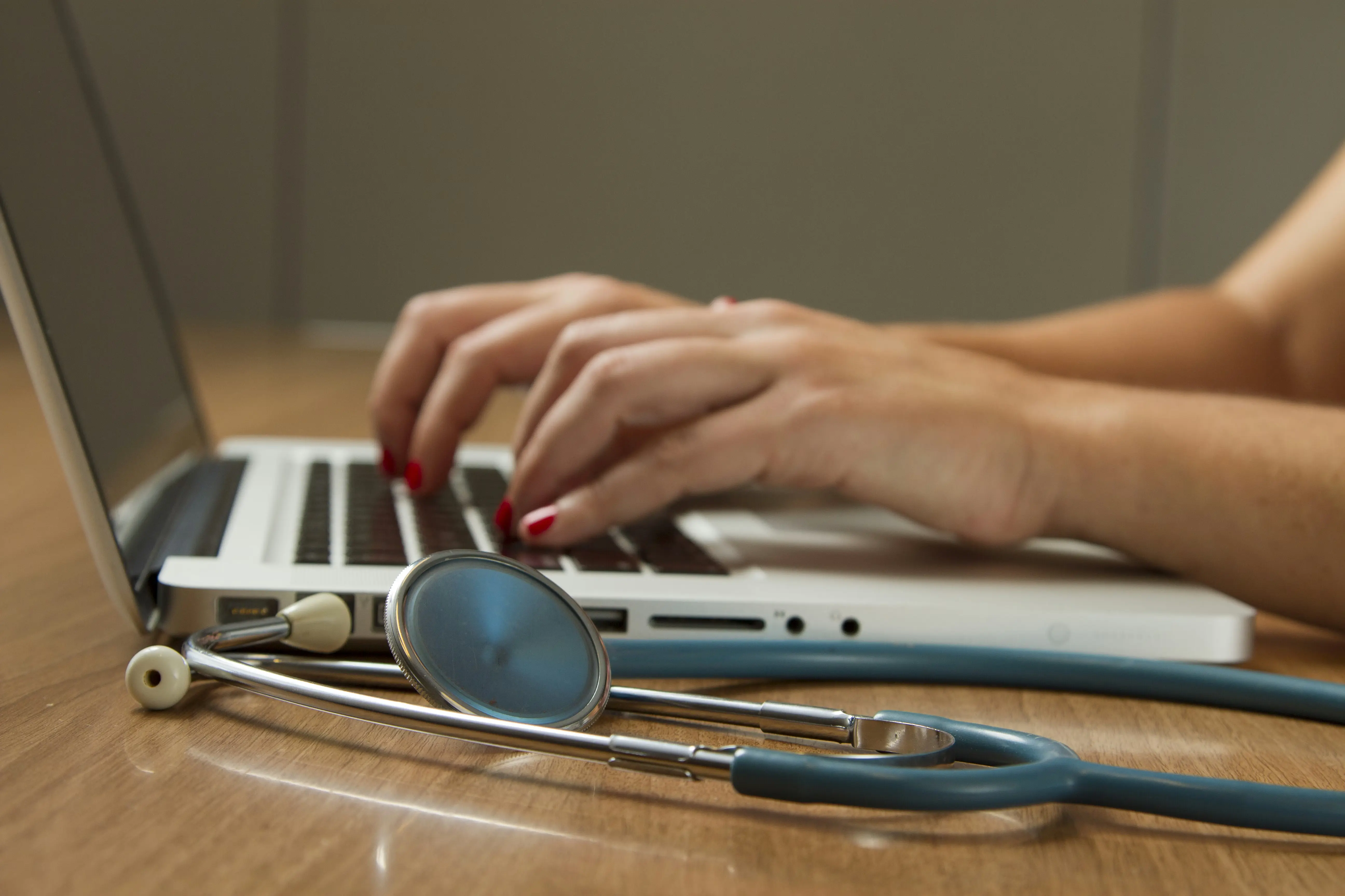 A clinician working at a laptop with a stethoscope on the desk